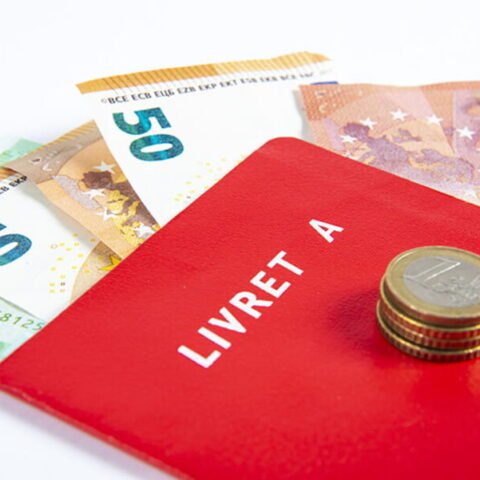 Un livret rouge marqué "Livret A" posé sur des billets de 50 euros et 100 euros avec quelques pièces, illustrant une solution classique d'épargne bancaire en France.