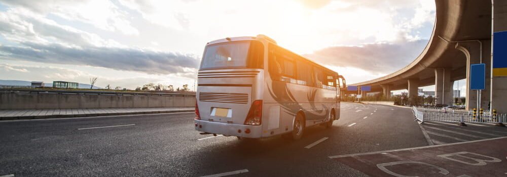 Autocar de tourisme gris argenté circulant sur une route asphaltée au soleil couchant, idéal pour la location d'autocar en Île-de-France.