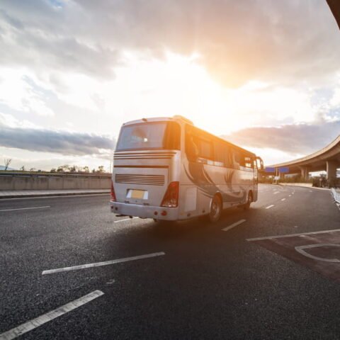 Autocar de tourisme gris argenté circulant sur une route asphaltée au soleil couchant, idéal pour la location d'autocar en Île-de-France.