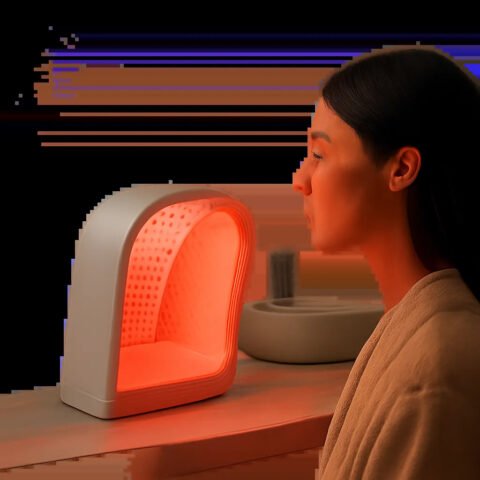 Une scène premium et minimaliste illustrant l’usage d’un appareil de lumière rouge pour le visage. L’ambiance évoque le soin à domicile, la simplicité d’usage et la crédibilité scientifique.