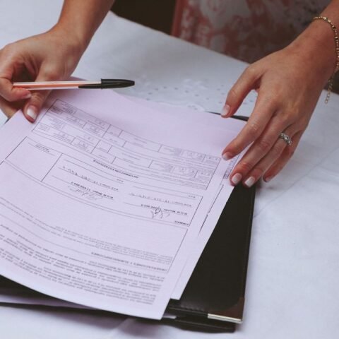 Deux mains signent un document sur une table, un stylo et un classeur à dossiers sont présents