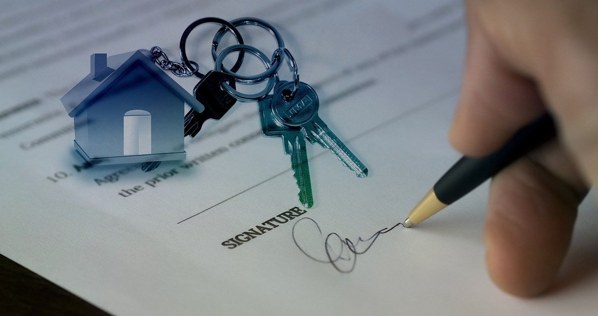 Clés de maison sur un document signé, main tenant un stylo au-dessus Clés de maison sur un document signé, main tenant un stylo au-dessus