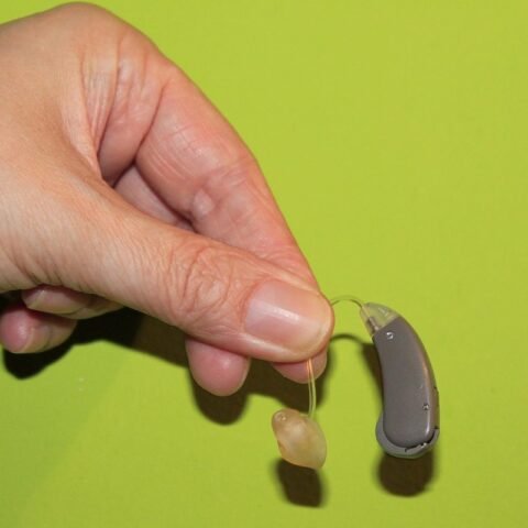 Une main tient un appareil auditif et un embout auriculaire