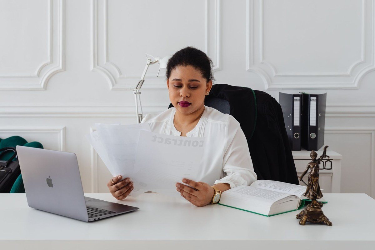 Femme lit des documents dans un bureau avec un ordinateur portable et une statue
