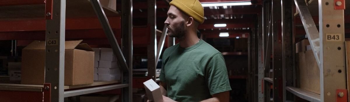 Homme inspecte des boîtes dans un entrepôt avec des étagères métalliques