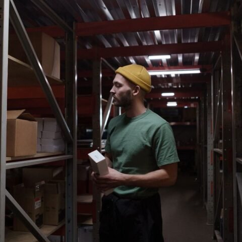 Homme inspecte des boîtes dans un entrepôt avec des étagères métalliques