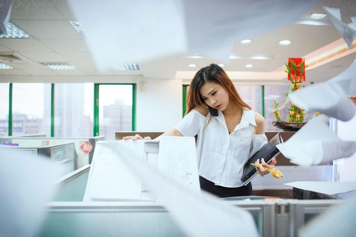 Femme en chemise blanche examine des documents dans un bureau moderne avec collègues