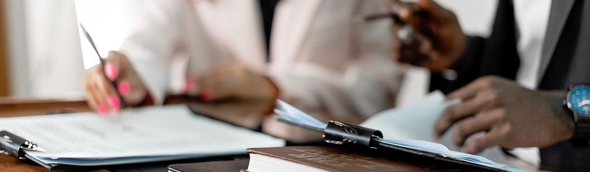 Deux individus signent des documents sur une table avec des livres et des dossiers