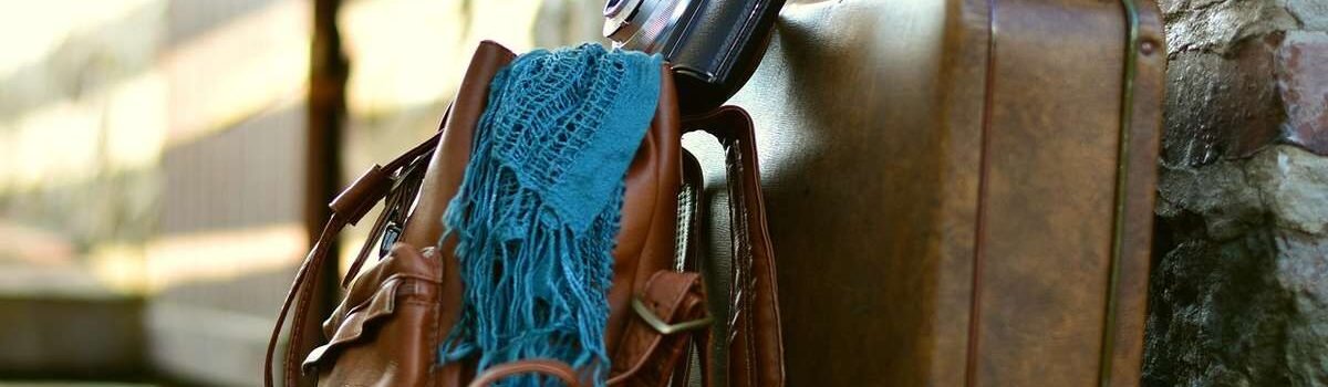 Sac en cuir, écharpe bleue, appareil photo et valise contre mur de pierre