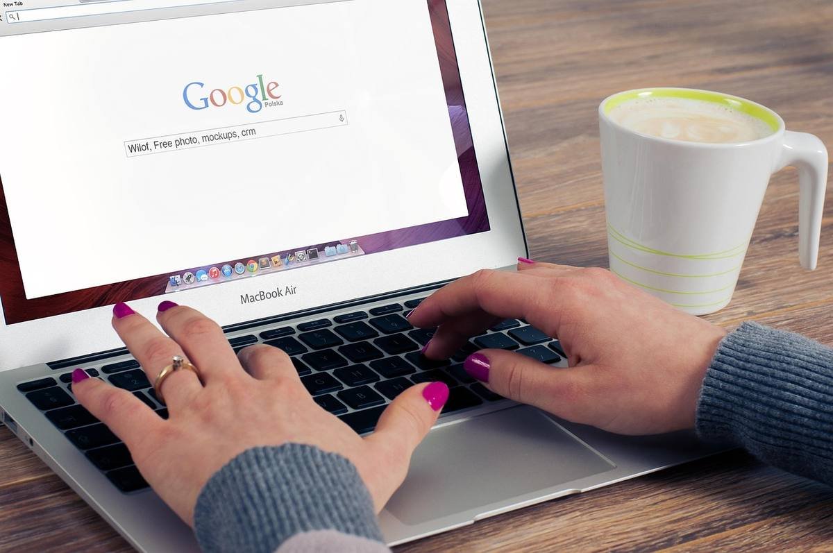 Main sur clavier d'ordinateur portable, Google, tasse à café, table en bois