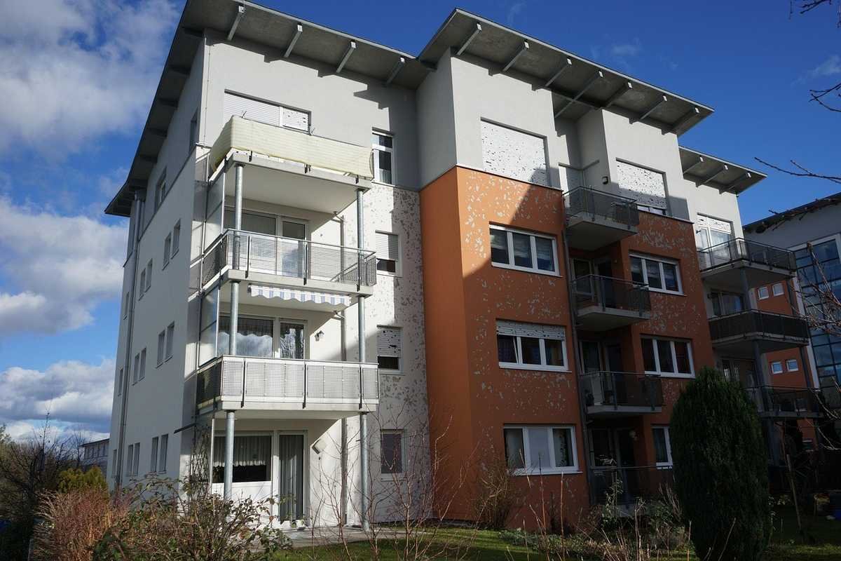 Immeuble blanc et orange à trois étages avec balcons et végétation sous un ciel bleu