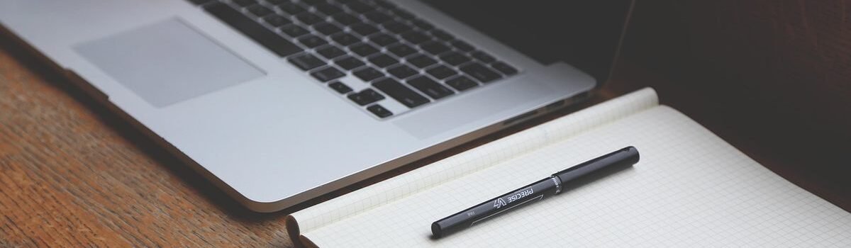 Un ordinateur portable ouvert à côté d'un cahier et d'un stylo sur du bois